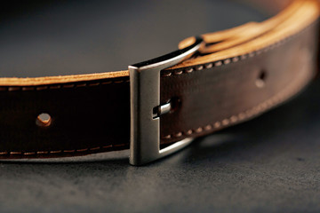 Brown belt made of genuine brown leather handmade on a dark background.