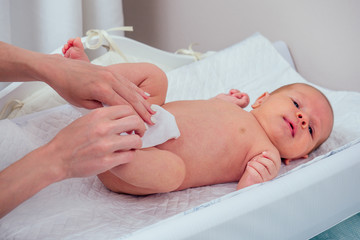 caucasian mother using wet wipes,applying baby powder before putting diapers on her four month old...