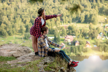 young pleasant girl pointing at the distance, girl showing direction to her boyfriend while resting on the mountain , full length side view photo. copy space