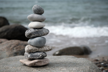 Ein aus acht flachen Steinen aufgebauter Turm, der auf einem am Strand liegenden Felsstein...