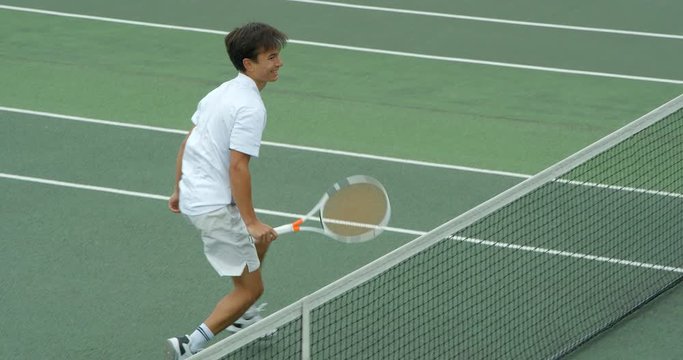 A mixed race tennis player runs across court, volleys over the net , smiles and celebrates.