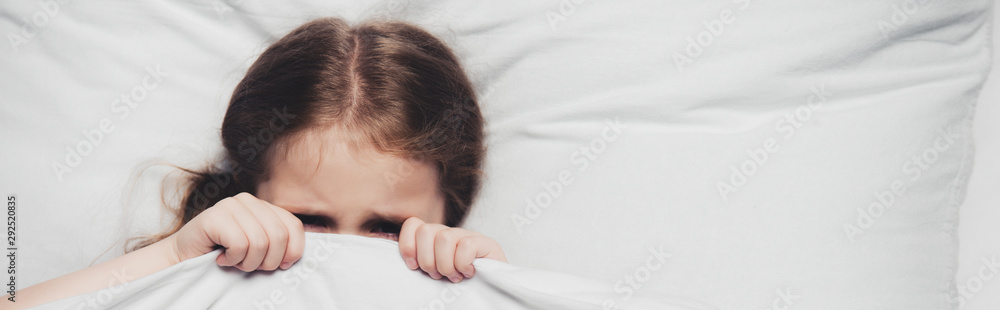 Wall mural panoramic shot of scared child hiding under blanket