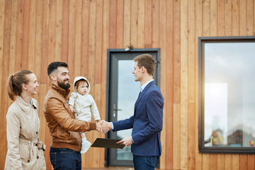 Caucasian happy family and realtor stand outdoor near new house just sold. Men shake hands.