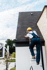 repairman in uniform and helmet repairing roof while standing on ladder © LIGHTFIELD STUDIOS