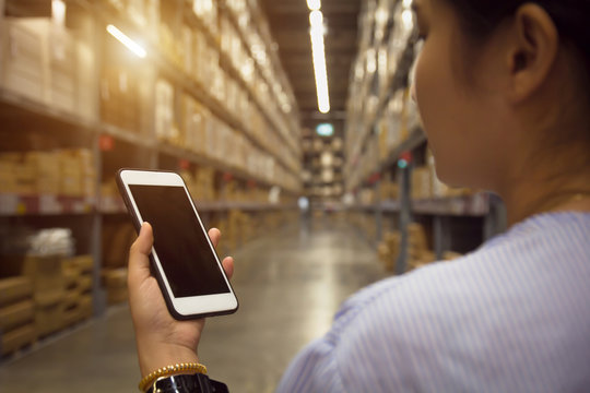 Young modern woman using touch screen mobile phone in warehouse storage.