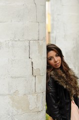 A girl with long hair in a dark leather jacket and pink dress stands thinking at the marble white column.