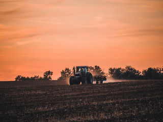 Fototapeta premium Tractor on filed by sunset.