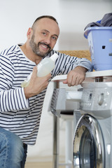 man loading clothes into washing machine in kitchen
