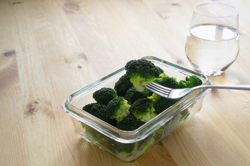 Steamed boiled broccoli on a fork in a glass container and pure water on a wooden background with copy space. Proper nutrition, super food and fitness