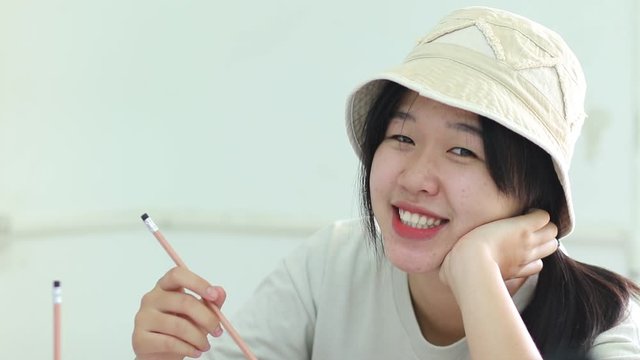 Smiling Beautiful Asian student girl daydreaming in high school classroom or reading book alone in class at front whiteboard at looking happiness in study, Education learning by myself