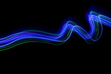 Long exposure photograph of neon multi colour in an abstract swirl, parallel lines pattern against a black background. Light painting photography.