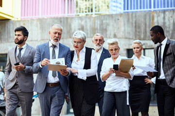 Seven businessman walking down the street and discussing project. Five of them blond, two brunettes