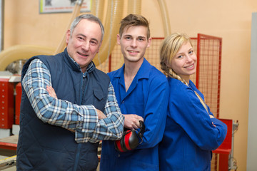mechanic and apprentices in a garage looking to camera