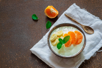 Greek yogurt with orange and a banana mint in a rustic bowl on on rusty metal wall , food and healthy meal concept, top view, copy space.