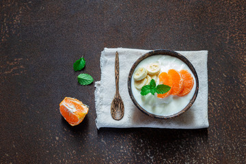 Greek yogurt with orange and a banana mint in a rustic bowl on on rusty metal wall , food and healthy meal concept, top view, copy space.