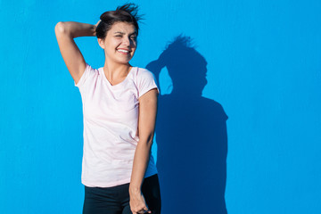 Beautiful cheerful young girl wearing casual clothes standing isolated over blue background on a sunny day. Woman smiling and hanging her hair. People and emotions image concept with copy space.