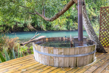 Leisure time at an idyllic wooden hot tub inside a fantasy green scenery with Caburgua river stream flowing inside an amazing rainforest full of trees during morning time a moody atmosphere background