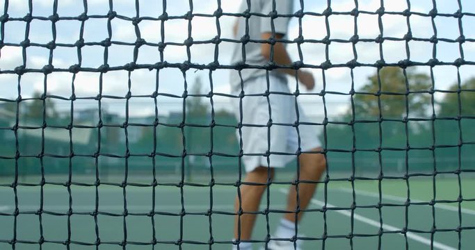 A Tennis player plays a shot and hits the net throwing his racket and kicking the air in frustration.