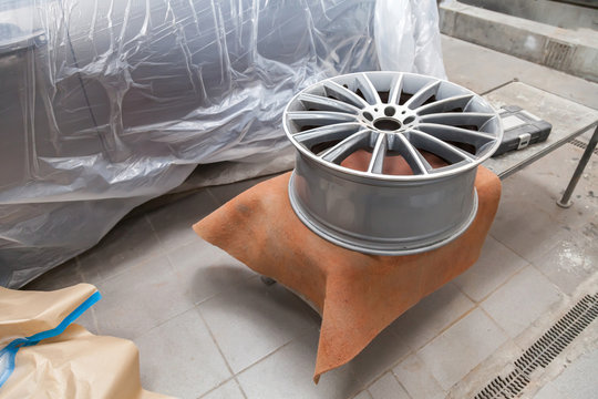 Preparing the surface of the aluminum disk of the car for subsequent painting in the workshop, cleaning and leveling the wheel with the help of abrasive material. Auto service industry.