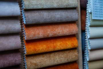 Pieces of textile material for interior trim and furniture making for example in the catalog of different colors for the design studio. Many colored materials hanging on the wall in stock.