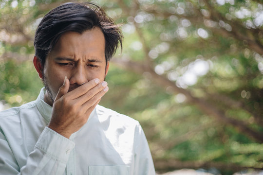 Halitosis , Young Asian Man Is Checking His Breath With His Hands. Mouth Health Problems