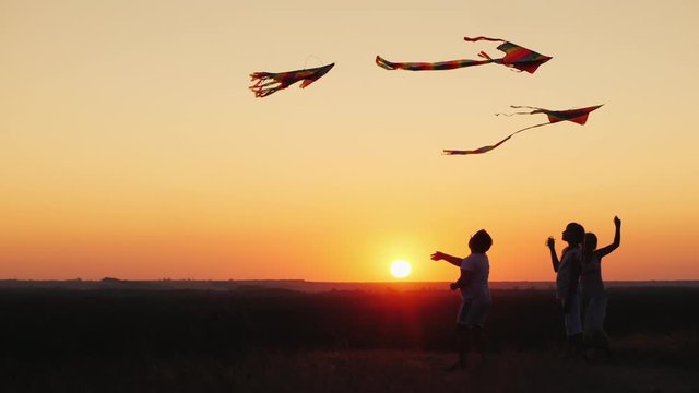 Children with mom play a kite at sunset on a summer evening. Active parents and children