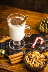 Traditional winter eggnog in glass mug with milk, rum and cinnamon, supper and Christmas decorations. Hot drink for the winter.