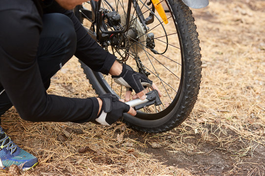 Close up of man hands pumping bicycle wheel, home maintenance of bike, bicycle service and maintaining for new season, faceless picture of wheel with flat tire, male reparing his bike in open air.