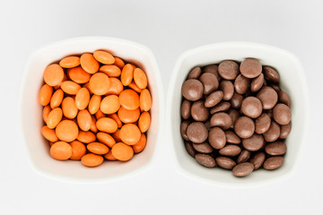 Two squared bowls with small orange and brown coated chocolate candies similar to m&ms in a squared bowl isolated on white background, top view