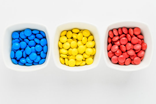 Three squared bowls with small red, yellow and blue coated chocolate candies similar to m&ms in a squared bowl isolated on white background, top view,  Romania flag colors