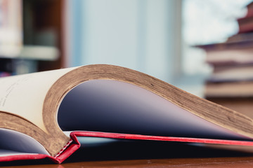 Opened textbook with blur bookshelf and book stack as background in library. Photo concept of education, knowledge, traditional learning, and literature. Selective focus