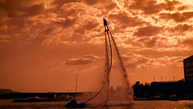 man is practicing flyboarding in sunset time on sea, moving over water surface on flows