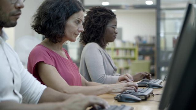 Group of people working with computers at library. Row of users sitting at table with computers. Technology concept