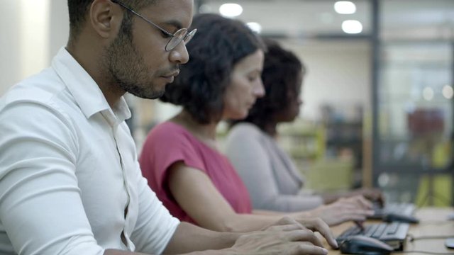 Serious employees working with computers at office. Row of people sitting at table and using computers. Technology concept