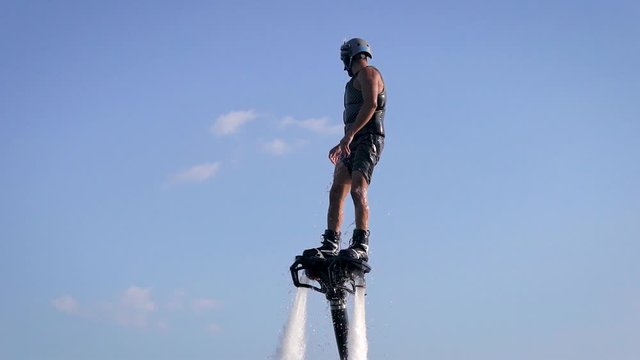 sportsman is practicing flyboarding on sea in summer vacation, close-up of body against blue sky