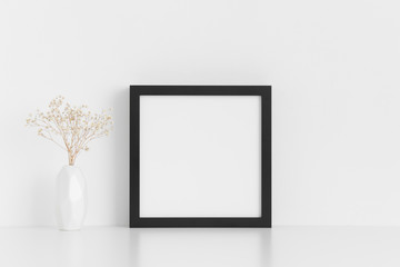 Black square frame mockup with a gypsophila in a vase on a white table.