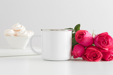 Enamel mug mockup with a book and a bouquet of pink roses on a white table.