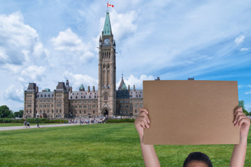 Protest concept, asian boy holding a blank protest sign in front of Canadian parliament in Ottawa