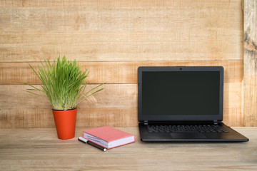 Open laptop, notebook and pen. Home workplace. Green houseplant on the table. Wooden background.