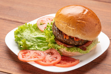 Homemade cheeseburgers with lettuce and tomato in a white plate on wooden background