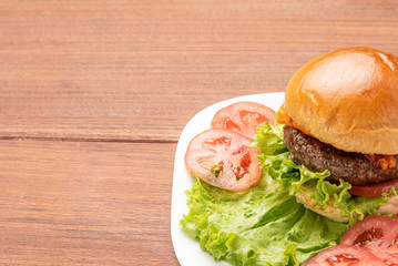 Homemade cheeseburgers with lettuce and tomato in a white plate on wooden background