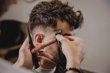 Deurstickers Jonge man met trendy kapsel bij kapperszaak. Kapper doet het kapsel en baard trimmen. © romaset