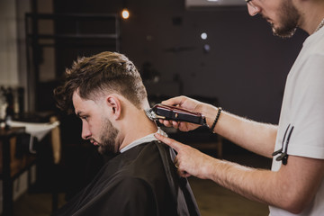 Young man with trendy haircut at barber shop. Barber does the hairstyle and beard trim.