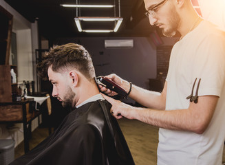 Young man with trendy haircut at barber shop. Barber does the hairstyle and beard trim.