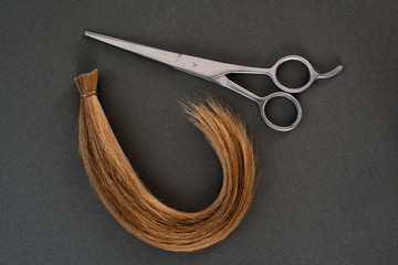 Cropped curl of blond and scissors. Black background. Close-up