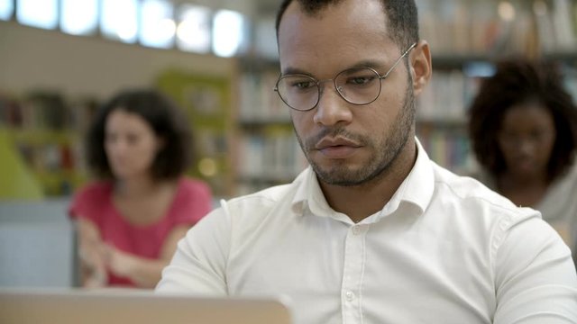 Closeup shot of focused young man using laptop at library. Handsome African American student studying at library. Education concept