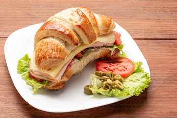 Croissant sandwich with salad, ham, cheese, tomatoes and olives on wooden background. Morning breakfast concept. Healthy and fast food. Isolated.
