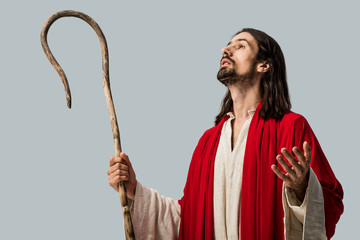 bearded man in jesus robe holding wooden cane and gesturing isolated on grey
