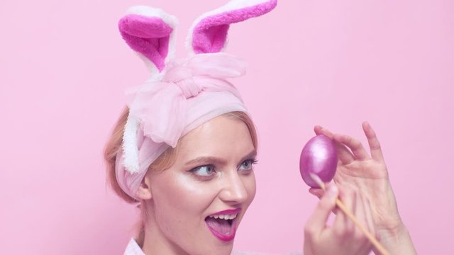 Sexy pin up woman with mask Easter bunny on a pink background and looks very sensually. Egg hunt and painting egg. Rabbit retro girl. Bunny pin up woman - close up.