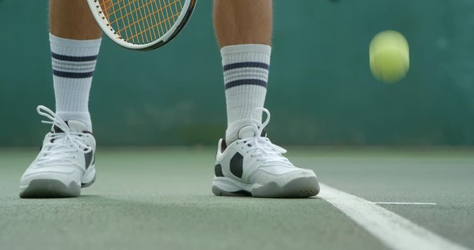 A Tennis player bounces the ball at the baseline in readiness to serve.